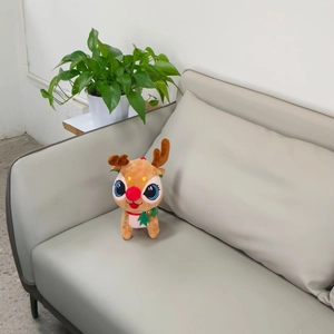 Cute Christmas reindeer plush toy with red nose and bell on a sofa, festive gift idea