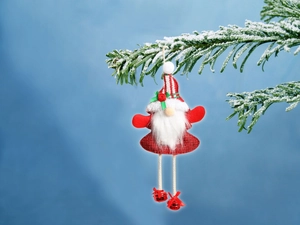 Detail of fabric Christmas gnome ornament with striped hat and bell hanging on snow pine branch