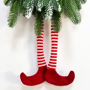 Detail of red and white striped elf legs hanging with frosted green pine branches