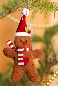 Detail of plush gingerbread man ornament with red scarf on a green Christmas tree branch