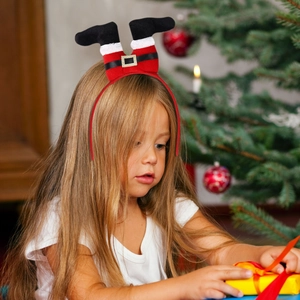 Girl wearing Christmas elf legs headband opening a gift box by a festive tree