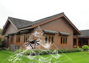 Outdoor Halloween decoration featuring a giant black plush spider on a large triangular web