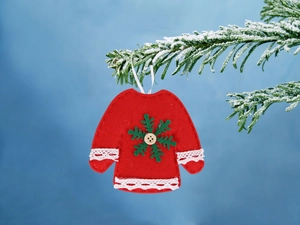 Mini maglione in feltro rosso con bottone in legno appeso a un ramo di pino innevato