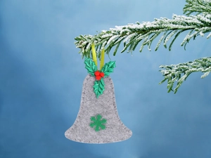 Dettaglio campana di Natale in feltro grigio con foglie di agrifoglio su ramo innevato