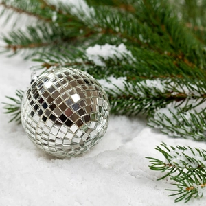 Silver mirror disco ball ornament on white snow with festive green pine branches background
