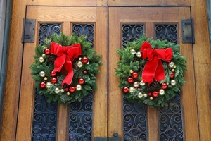 Christmas wreaths with red bows, gold baubles, and pine cones on a wooden door