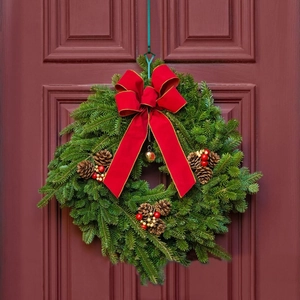 Christmas wreath with red velvet bow, pine cones, and berries on a dark red door