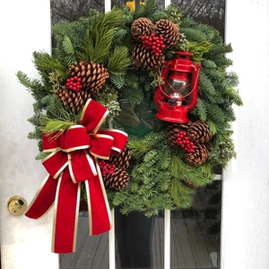 Christmas wreath with red bow, pine cones and lantern on white wooden door