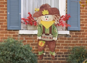 Close-up of harvest scarecrow doll holding Happy Fall banner with straw and fabric details