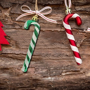 Red and green Christmas cane ornaments with glitter and bows on wood background