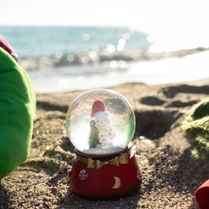 Christmas snowman glass snow globe with red resin base and mini tree on summer beach