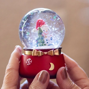 Christmas snowman glass snow globe with red base and golden bow on a hand palm