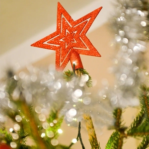 Macro detail of red glitter star tree topper with 3D hollow design on festive tree
