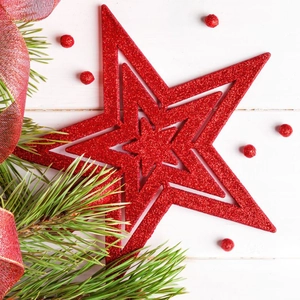 Detail of red glittered three-layer hollow star tree topper on white wood background