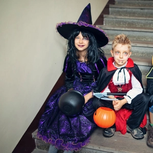 Children in purple witch costume and vampire cape with Halloween candy buckets and sickle