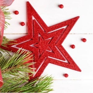 Three-layer red glittered Christmas star tree topper on a white wooden background