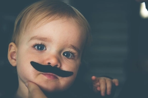Close-up of a funny black fake mustache sticker on a baby face for photo props
