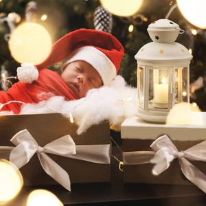 Close-up of baby in red velvet Christmas outfit with Santa hat inside a brown gift box