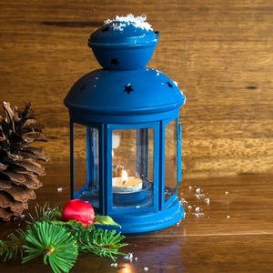 Detail of matte blue Christmas lantern with star cutouts, candle flame and faux snow