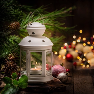 Close-up of a white metal lantern with star cutouts and a lit candle on Christmas table