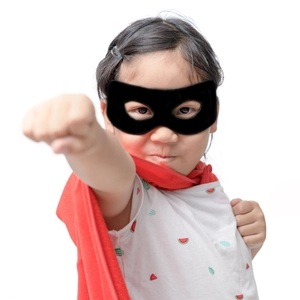 Close-up of a child wearing a black hero eye mask and a vibrant red cosplay cape