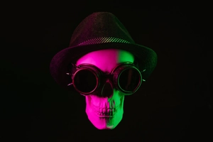 Steampunk goggles with metal spikes on a skull wearing a black top hat under neon light