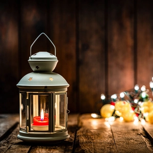 Close-up of a white vintage star lantern with a lit red candle on a rustic wood surface