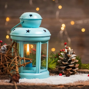 Close-up of blue hollow star lantern with pine cones and berries on snowy wood surface