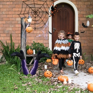 Outdoor Halloween decor showing striped witch legs stakes and carved pumpkins on the lawn