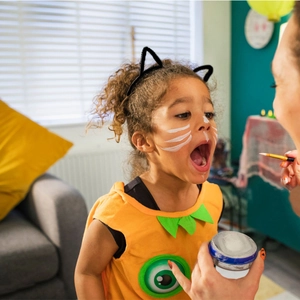 Applying white face paint on a child with cat ears for Halloween makeup party