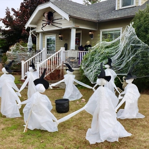 Outdoor Halloween decor with white fabric ghosts in witch hats around a black cauldron