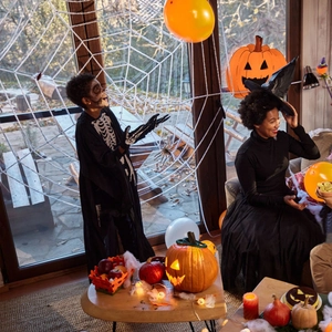 Cozy Halloween home party scene with spider webs, pumpkin lights and festive costumes