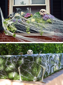 Outdoor Halloween decor detail featuring stretchy spider webs with skulls on green plants