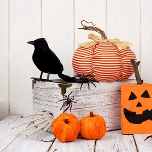 Halloween decor set with black feathered crow, striped pumpkins, and skeletal hand on white wood
