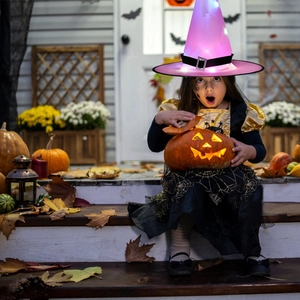 Girl wearing a glowing purple Halloween witch hat with LED lights and spiderweb dress