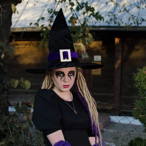 Detail of black velvet witch hat with purple ribbon and gold buckle in forest