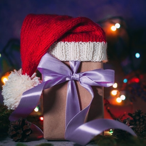 Close-up of a festive gift box with a knit Christmas hat and large purple satin ribbon