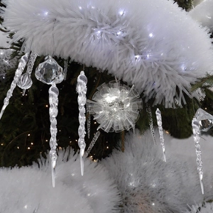 Detail of clear acrylic icicle and geometric sphere ornaments on a snowy Christmas tree
