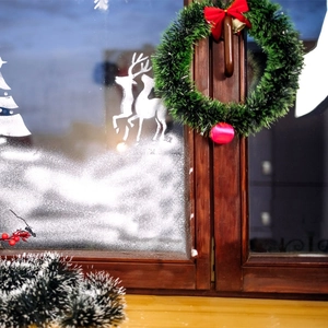 Christmas wreath with red bow and gold bells hanging on a window with reindeer snowflake decals
