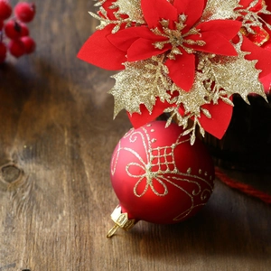 Detail of red frosted Christmas ball with gold glitter patterns and silk poinsettia flower