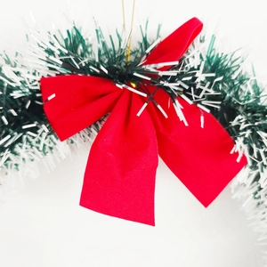 Close-up of green Christmas tinsel garland with white tips and a large red ribbon bow