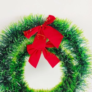 Lush green Christmas tinsel wreath featuring two vibrant red bows for holiday door decor