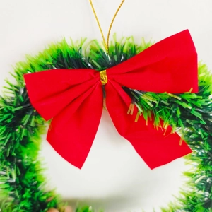 Close-up of a lush green Christmas tinsel wreath featuring a large vibrant red bow