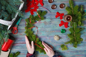 Flat lay of DIY Christmas wreath kit with red bows and evergreen branches on blue wood