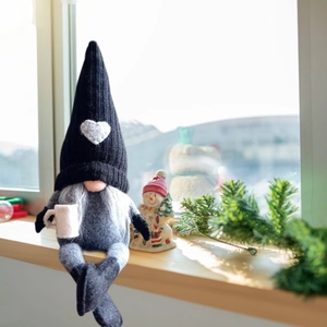Nordic Christmas gnome doll with heart knit hat sitting on a bright wooden windowsill