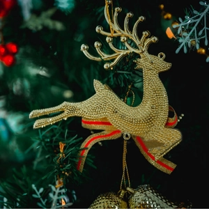 Sparkling gold Christmas reindeer ornament with red ribbon hanging on a festive tree branch