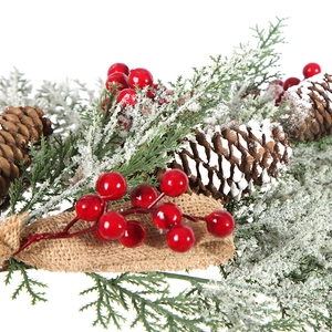 Detail of Christmas garland with pine cones, red berries, snowy needles and burlap bow