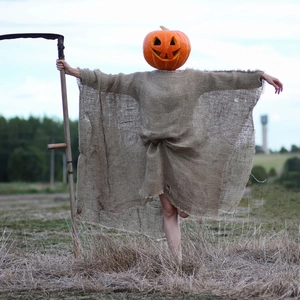 Creepy scarecrow costume with jack-o'-lantern pumpkin mask and burlap robe in field