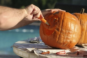 Close-up of orange handle serrated carving knife detailing a Halloween pumpkin