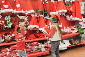 Children selecting colorful plush Christmas hats and elf ears in a festive market scene